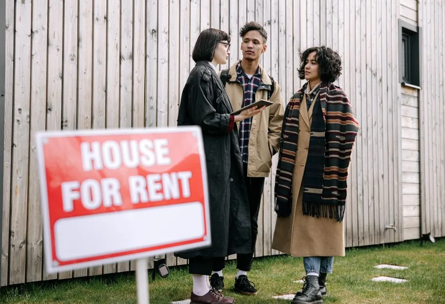 Prospective tenants and a letting agent discussing a rental property beside a House For Rent sign Prospective tenants and a letting agent discussing a rental property beside a House For Rent sign
