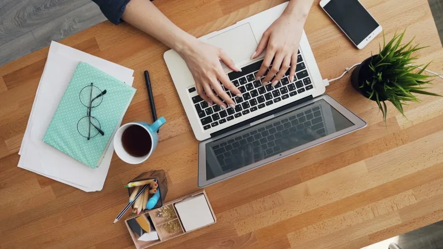 A UK online seller working through cross-border sales admin at a tidy desk with laptop, notebook and tea