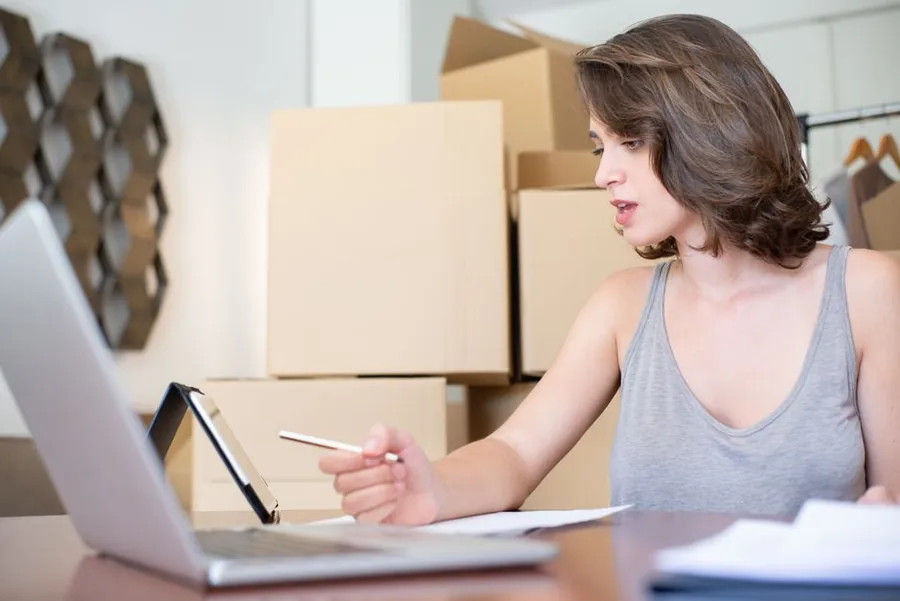 A home-based Shopify seller checking VAT registration details on a laptop beside stacked stock boxes A home-based Shopify seller checking VAT registration details on a laptop beside stacked stock boxes