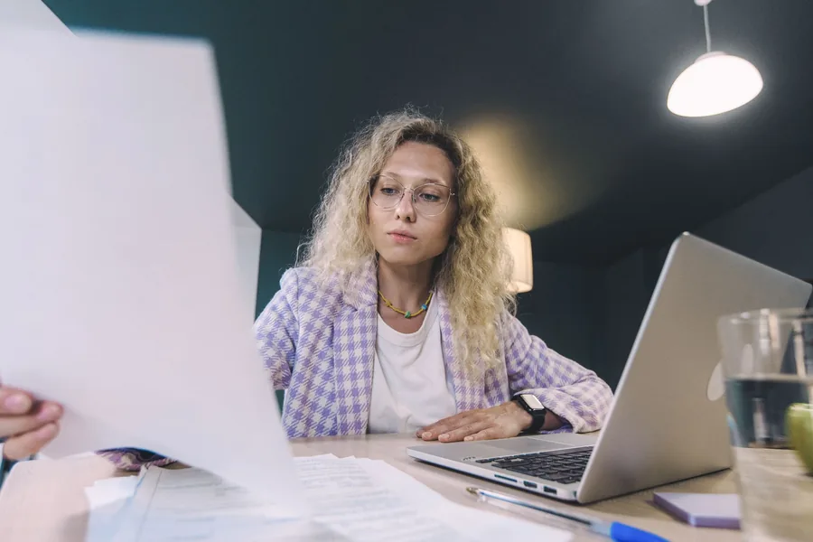 Small business owner reviewing documents at a laptop while deciding whether to change accountants Small business owner reviewing documents at a laptop while deciding whether to change accountants