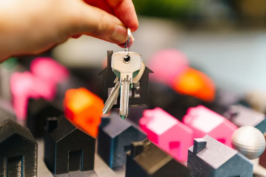 A hand lifting a house key above a cluster of model homes, representing a buy-to-let purchase subject to the stamp duty surcharge