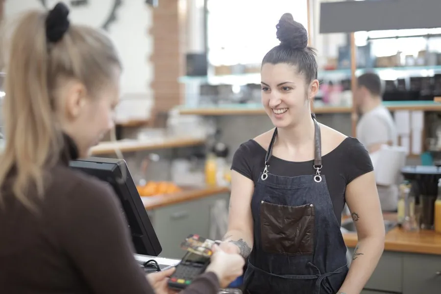 A small business employee taking a card payment at the counter, the kind of staff member entitled to statutory sick and holiday pay A small business employee taking a card payment at the counter, the kind of staff member entitled to statutory sick and holiday pay