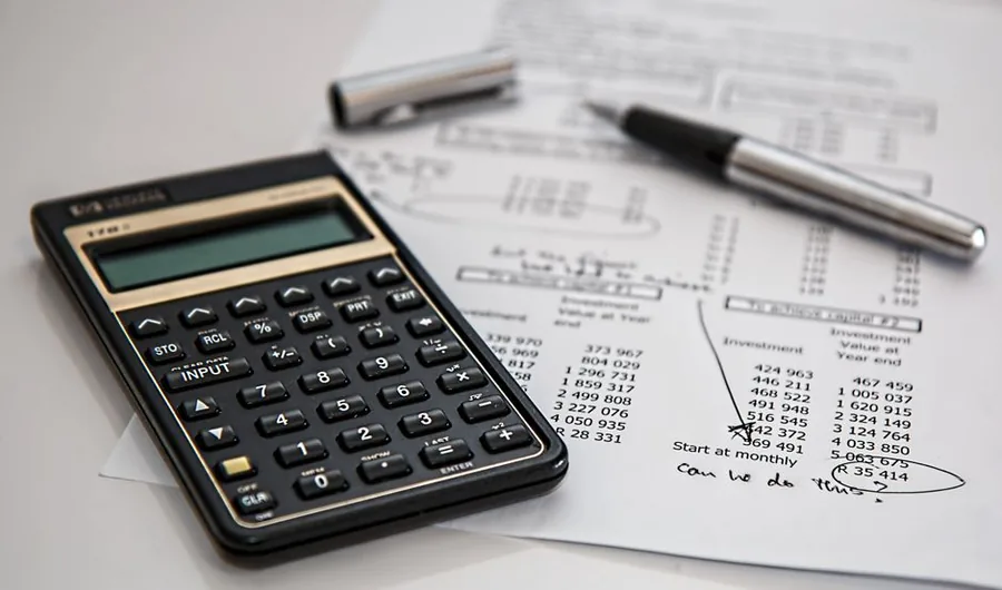 A calculator resting on printed ledger statements as a small business owner reconciles account balances by hand A calculator resting on printed ledger statements as a small business owner reconciles account balances by hand