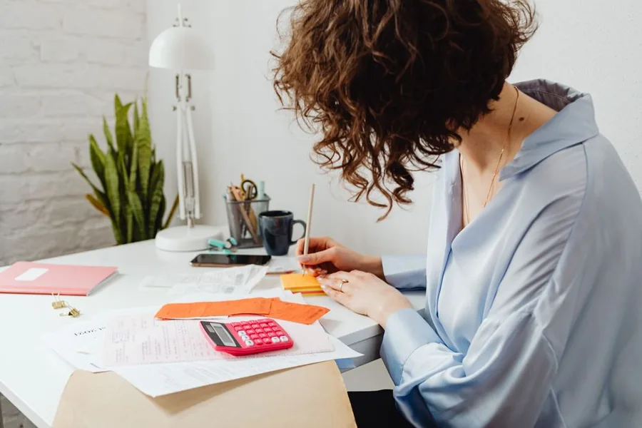 A company director working through take-home pay figures with a calculator and paperwork at a home office desk