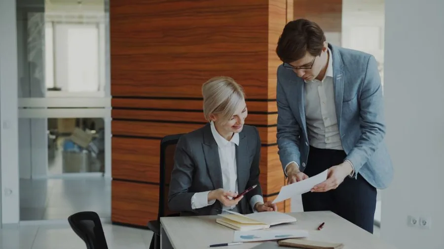 An employee reviewing a payroll form with an adviser at a laptop to check their tax code An employee reviewing a payroll form with an adviser at a laptop to check their tax code