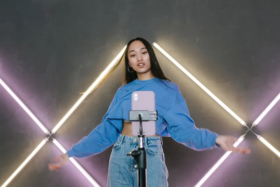 A TikTok creator recording a piece to camera on a phone tripod in a neon-lit home studio A TikTok creator recording a piece to camera on a phone tripod in a neon-lit home studio