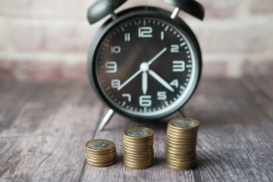 Stacks of UK pound coins rising in front of an alarm clock, reflecting savings interest building up over time Stacks of UK pound coins rising in front of an alarm clock, reflecting savings interest building up over time