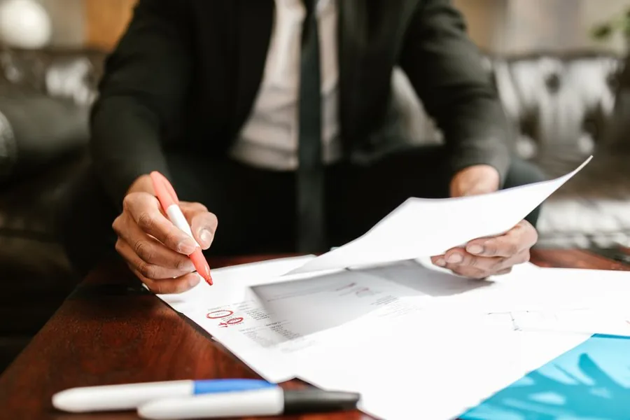 A UK adviser reviewing an employee's redundancy settlement paperwork with a red pen at a desk