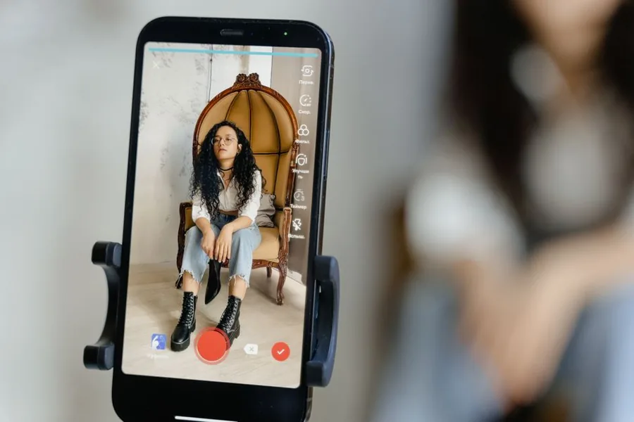 A UK TikTok creator recording a vertical video to a tripod-mounted phone under neon studio lighting A UK TikTok creator recording a vertical video to a tripod-mounted phone under neon studio lighting