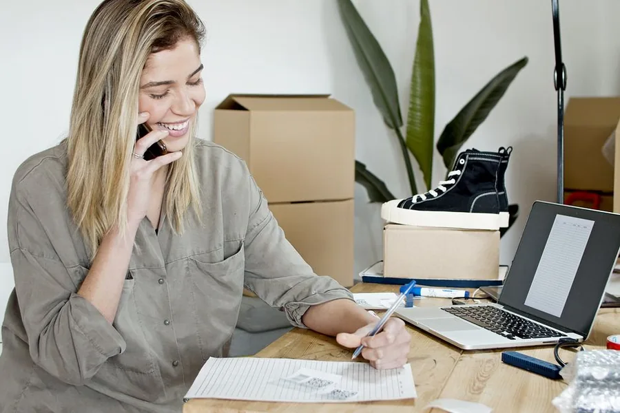 An online marketplace seller checking sales paperwork beside dispatch parcels and a laptop at a home workspace An online marketplace seller checking sales paperwork beside dispatch parcels and a laptop at a home workspace