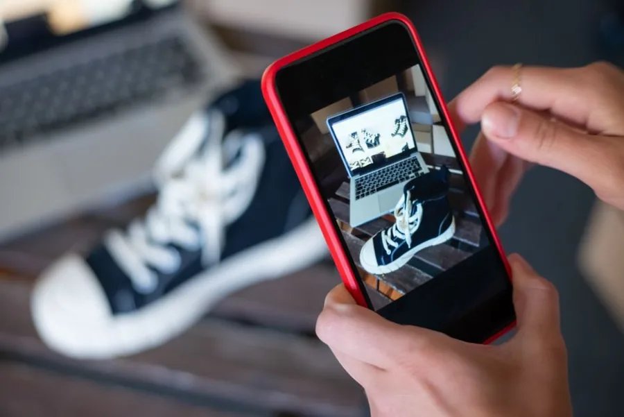 A TikTok Shop seller photographing a trainer on their phone to create a product listing for online sale A TikTok Shop seller photographing a trainer on their phone to create a product listing for online sale