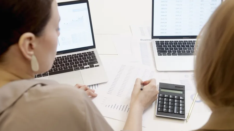 Two online sellers reconciling their sales figures on a calculator and spreadsheets before completing the VAT return Two online sellers reconciling their sales figures on a calculator and spreadsheets before completing the VAT return