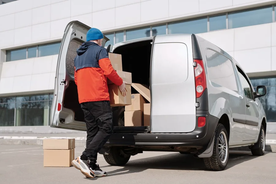 A courier loading cardboard parcels into the back of a van outside a business, a typical Great Britain to Northern Ireland goods movement A courier loading cardboard parcels into the back of a van outside a business, a typical Great Britain to Northern Ireland goods movement
