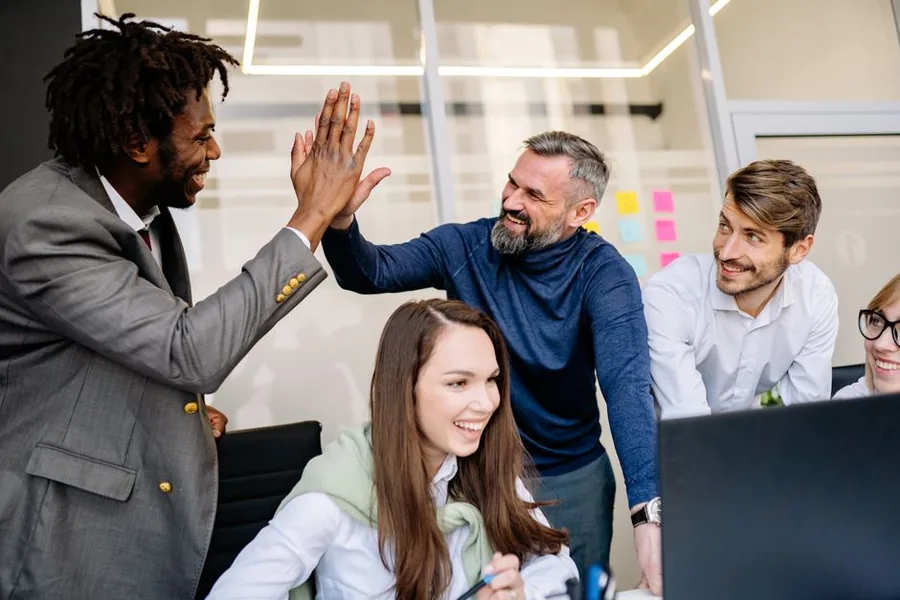 A cheerful UK office team high-fiving over a shared desk, reflecting the morale lift small tax-free trivial benefits can bring A cheerful UK office team high-fiving over a shared desk, reflecting the morale lift small tax-free trivial benefits can bring