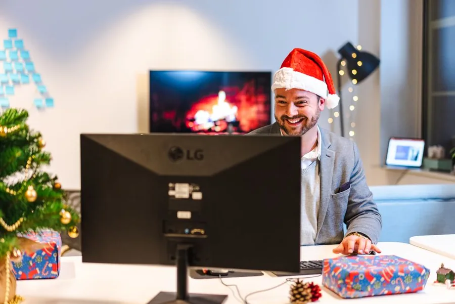 A UK office worker in a Santa hat with wrapped festive gifts on the desk, a classic trivial benefit perk A UK office worker in a Santa hat with wrapped festive gifts on the desk, a classic trivial benefit perk