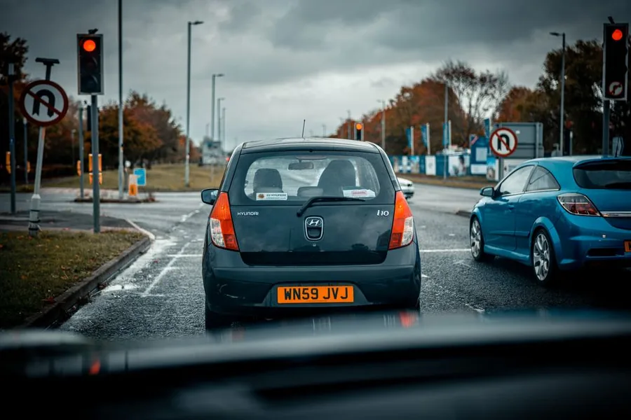 Traffic waiting at red lights on a wet UK junction, a car showing a yellow number plate beside British road signs Traffic waiting at red lights on a wet UK junction, a car showing a yellow number plate beside British road signs