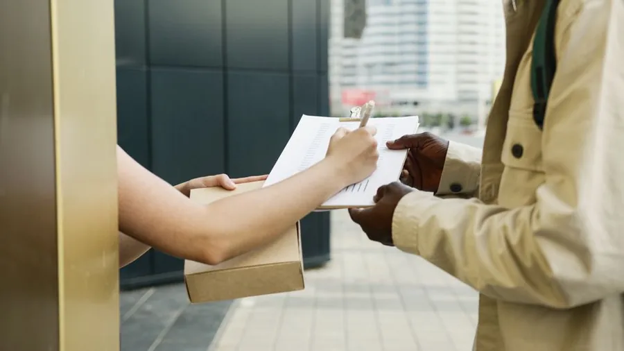 An ecommerce seller handing over a parcel and signing dispatch paperwork outside a city office An ecommerce seller handing over a parcel and signing dispatch paperwork outside a city office