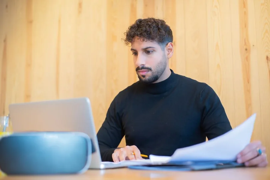 A UK contractor reviewing payslips and paperwork at a laptop while weighing umbrella against limited company options A UK contractor reviewing payslips and paperwork at a laptop while weighing umbrella against limited company options