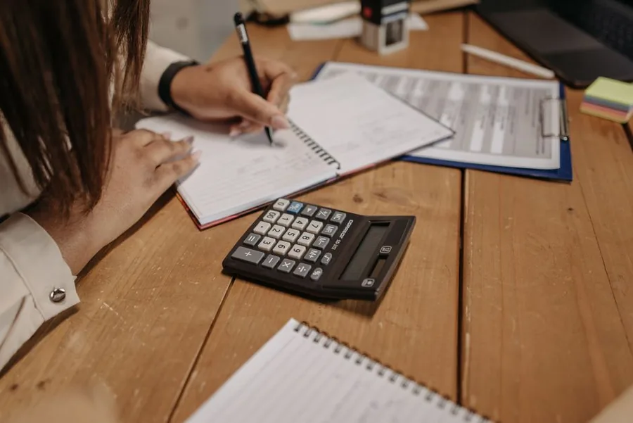 A small business owner running VAT figures on a calculator alongside invoices and a notebook to weigh up the Flat Rate Scheme A small business owner running VAT figures on a calculator alongside invoices and a notebook to weigh up the Flat Rate Scheme
