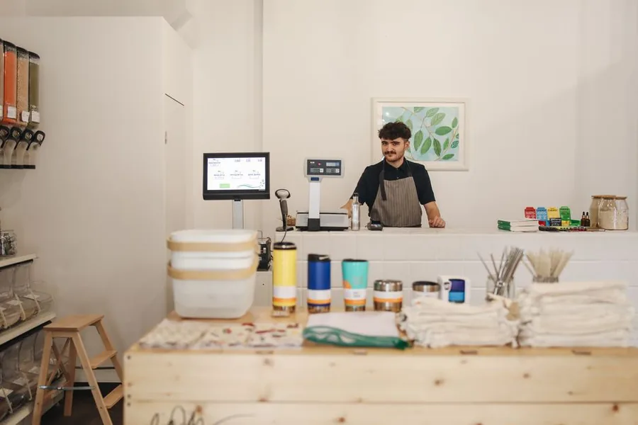 An independent shopkeeper at the till of a UK zero-waste store, the kind of small retailer that runs a VAT retail scheme An independent shopkeeper at the till of a UK zero-waste store, the kind of small retailer that runs a VAT retail scheme