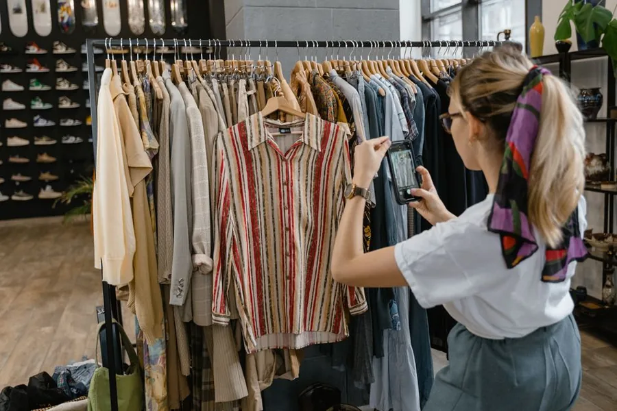 A reseller photographing secondhand clothing on a rack to list items for sale online A reseller photographing secondhand clothing on a rack to list items for sale online