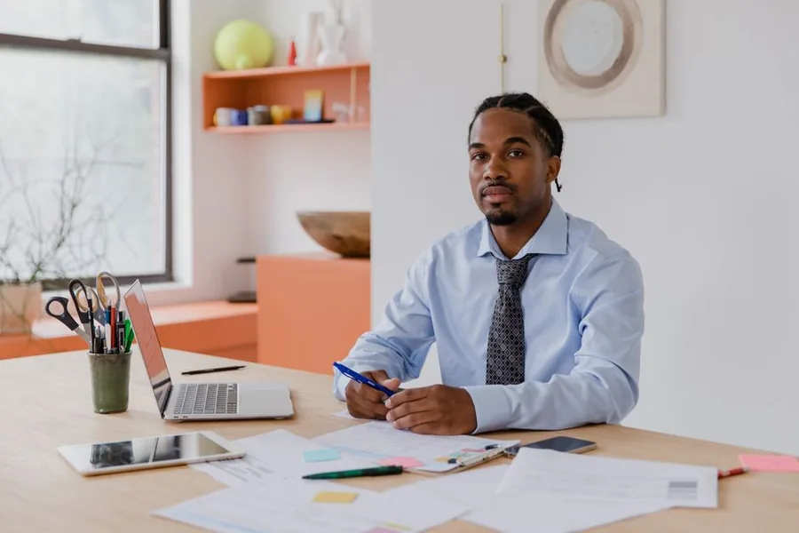A professional at a UK office desk reviewing paperwork and a laptop while checking tax reference details A professional at a UK office desk reviewing paperwork and a laptop while checking tax reference details