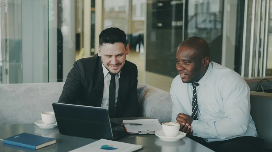 Two business owners discussing their company finances on a laptop over coffee in a modern office Two business owners discussing their company finances on a laptop over coffee in a modern office
