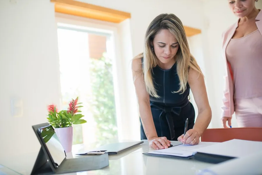 A business owner signing registration paperwork with her accountant in a bright office A business owner signing registration paperwork with her accountant in a bright office