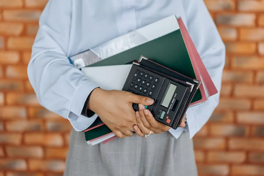 A UK bookkeeper carrying accounts folders and a calculator, ready to work out asset depreciation for a small business A UK bookkeeper carrying accounts folders and a calculator, ready to work out asset depreciation for a small business