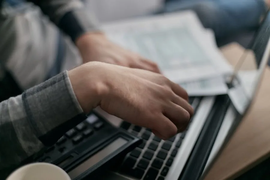 Working through invoices at a laptop with financial paperwork alongside, moving billing from paper to digital records Working through invoices at a laptop with financial paperwork alongside, moving billing from paper to digital records