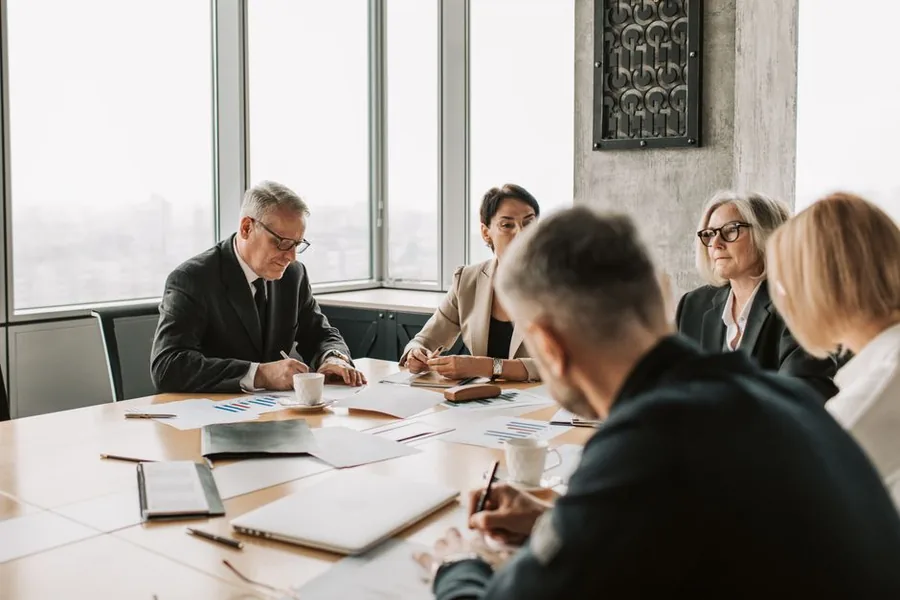 Company directors and shareholders reviewing financial reports together around a boardroom table Company directors and shareholders reviewing financial reports together around a boardroom table