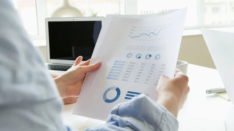 A small business owner reviewing printed sales figures alongside a laptop to work out what to report to HMRC A small business owner reviewing printed sales figures alongside a laptop to work out what to report to HMRC