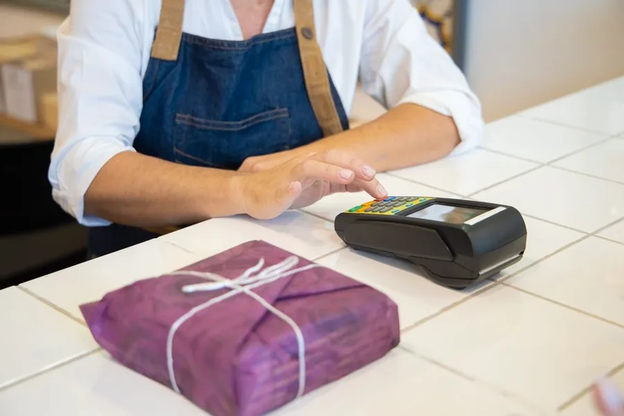 A shop owner taking a card payment for a wrapped parcel, the moment that fixes the VAT tax point on a sale