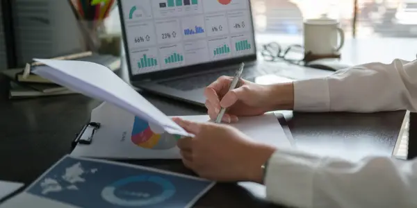 A businessperson is analyzing financial charts and strategies on a laptop while reviewing printed reports.