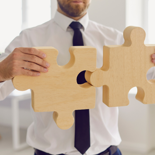 A person connecting two large wooden puzzle pieces, symbolizing collaboration and problem-solving.