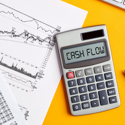 A calculator displaying "CASH FLOW" on its screen, placed on a yellow surface next to financial charts and documents, symbolizing accounting and financial analysis.