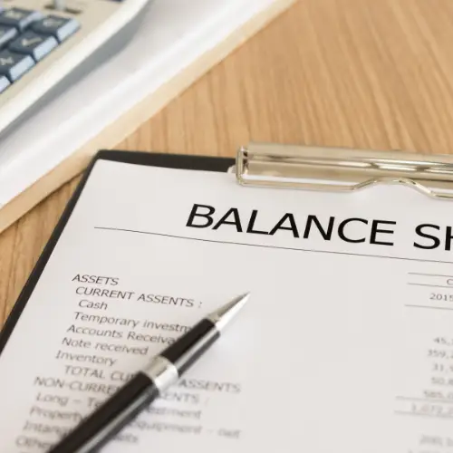 A close-up of a financial balance sheet with a pen and papers.