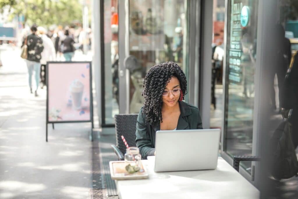 A woman working on a laptop in a cafe with paperwork spread out.