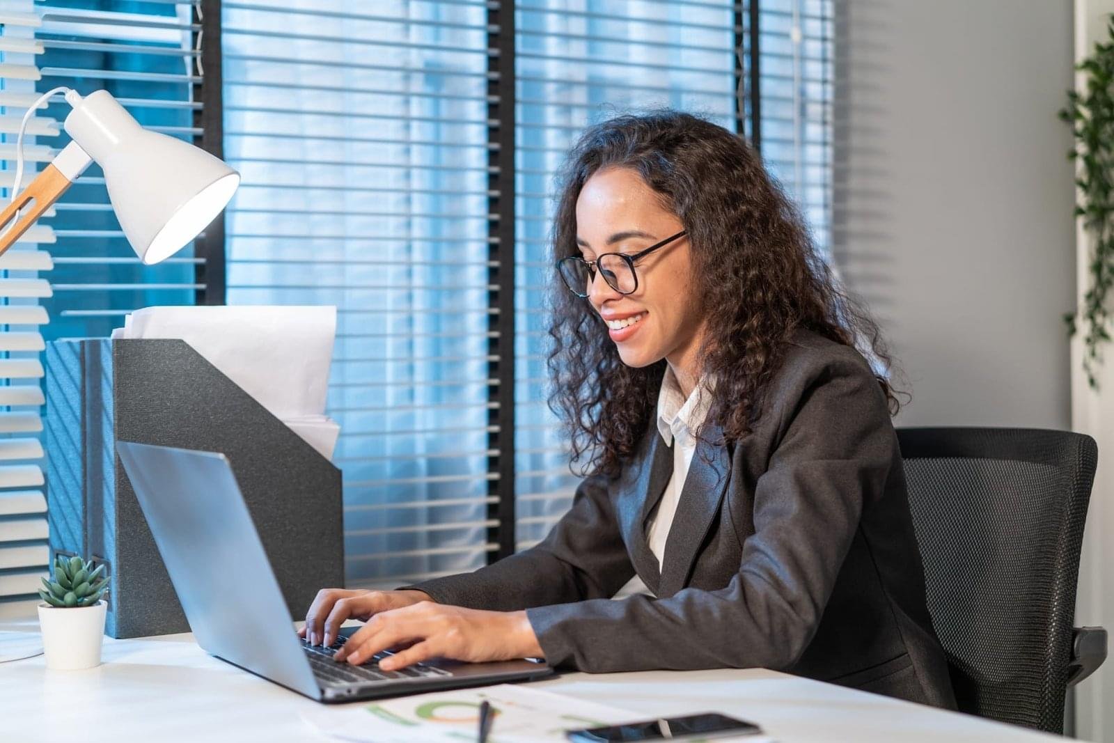 A business professional works on a laptop, analyzing financial data in an office setting.